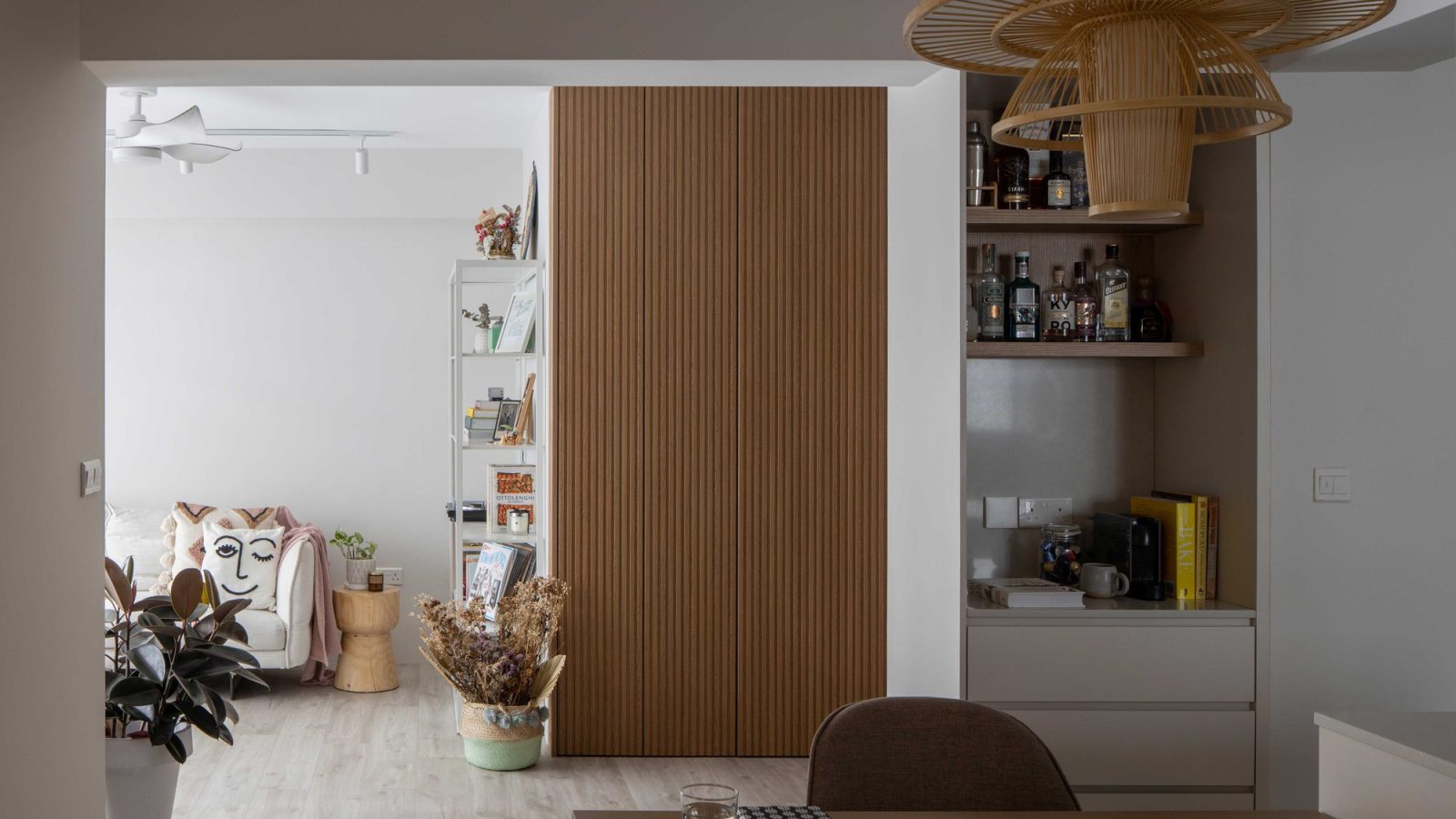 A tiered rattan pendant light hangs beside a reeded oak wardrobe door, with a built-in bar nook glimpsed through the opening.