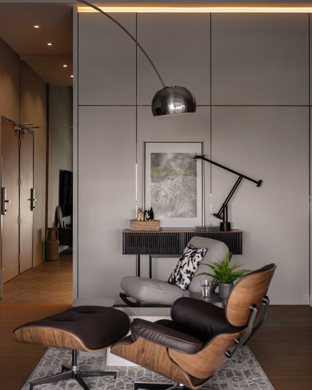 An Eames lounge chair and ottoman anchor a quiet reading corner, paired with an arc floor lamp and a slim console styled with framed art.