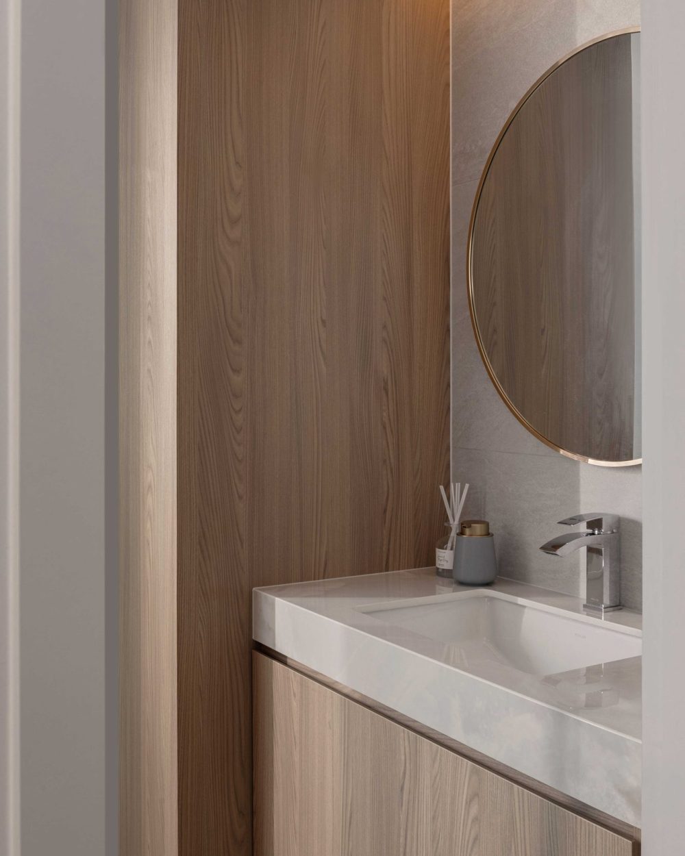 A brass-framed round mirror and warm timber panelling give the ensuite a soft, boutique-hotel finish.
