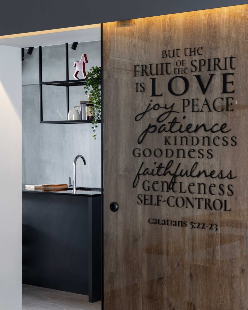 A verse from Galatians is carved into a warm timber sliding door, opening onto the kitchen's concrete-walled counter.