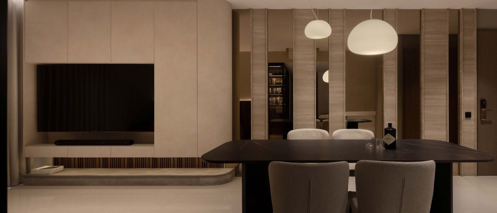 A pair of sculptural pendant lights hang low over the dining table, with the open-concept TV wall visible just beyond.