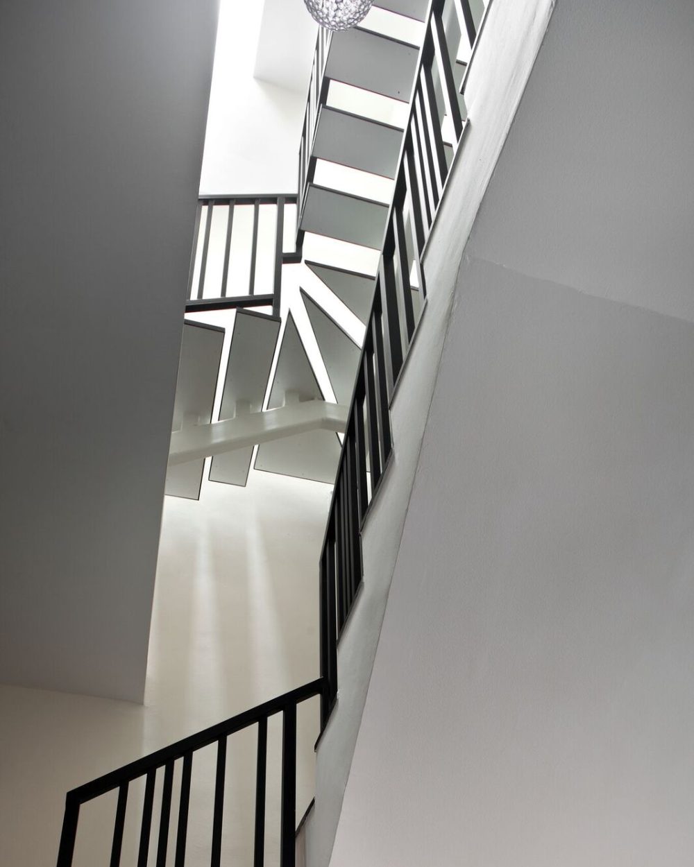 Black metal balustrades and crystal pendant lighting turn the staircase into a sculptural centrepiece within the stairwell.