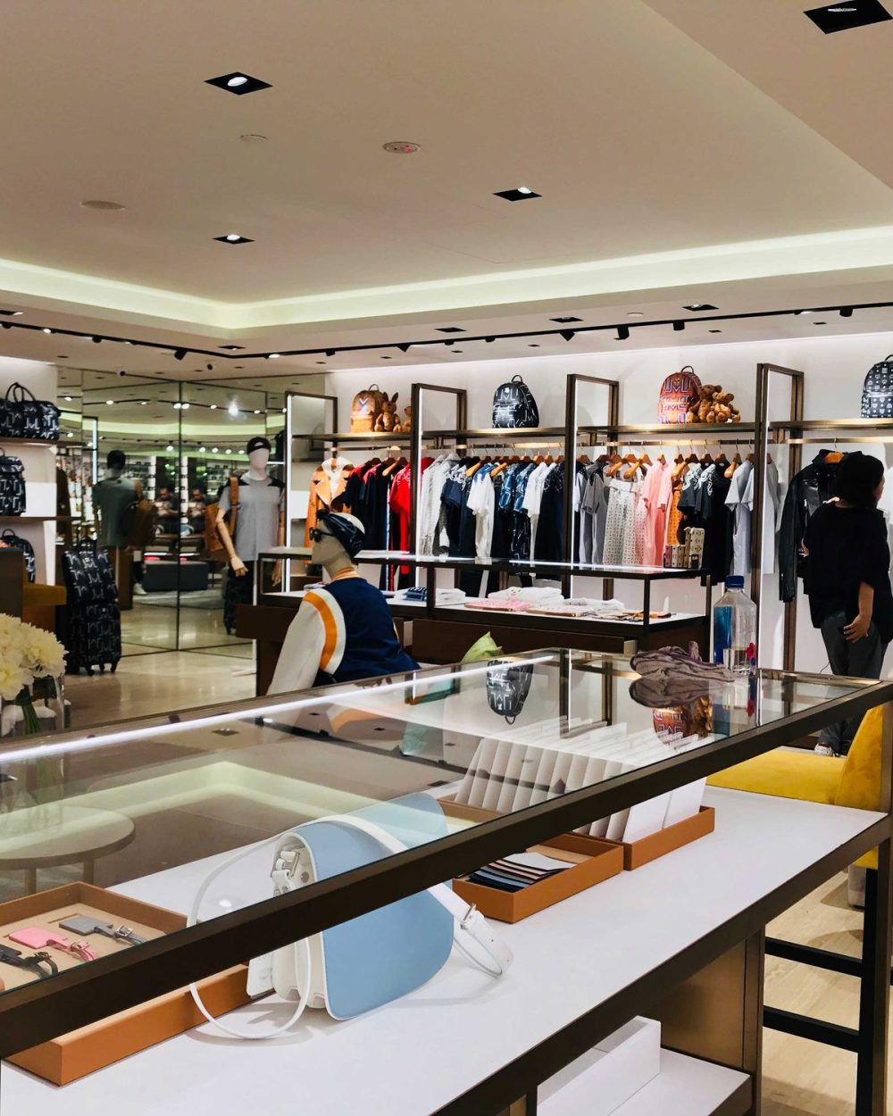 A mannequin in a striped sweater seated at a display counter amid backpacks and clothing racks.