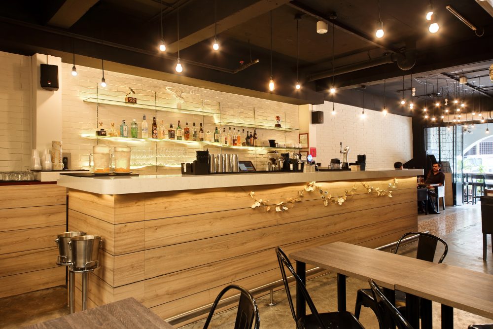 A second timber-fronted bar counter continues the whitewashed brick and string-light theme along the length of the space.