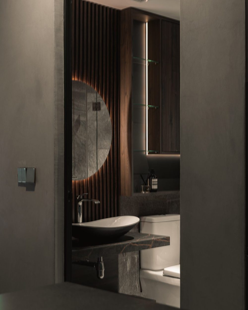 Glimpsed through a partly open door, a second bathroom repeats the same warm timber and dark stone palette.