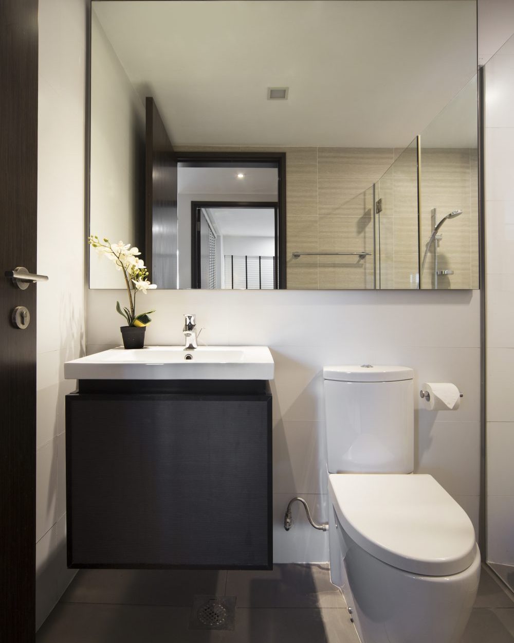 A dark vanity and floating mirror bring the same refined palette to the second bathroom, styled with a potted orchid.