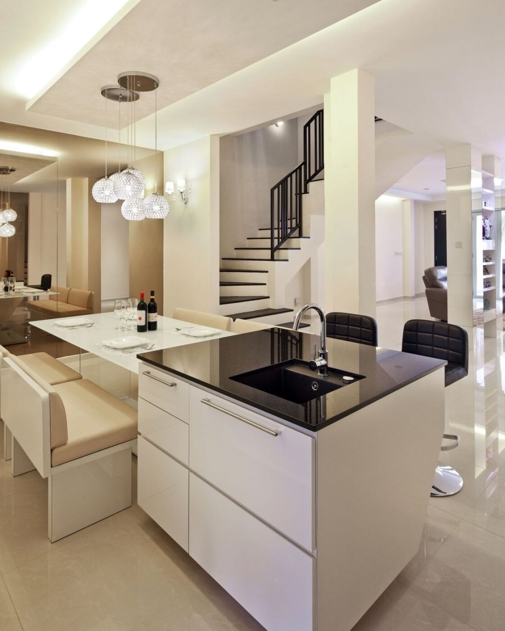 Black bar stools line the island's far side, with the staircase and crystal pendants visible in the mirrored wall beyond.