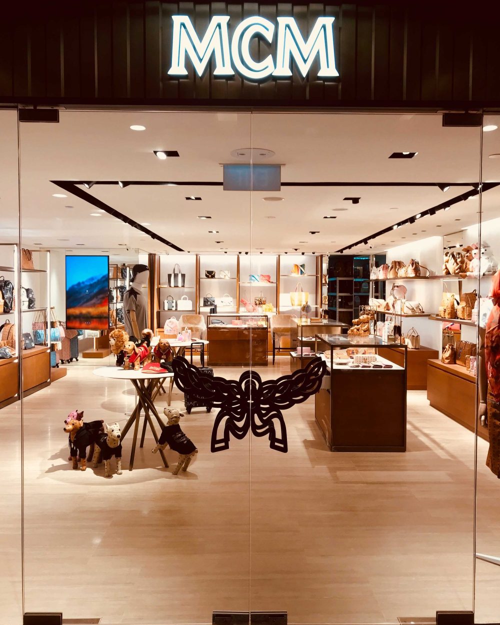 A straight-on view of the MCM storefront entrance with the illuminated logo and canine figures on the floor.