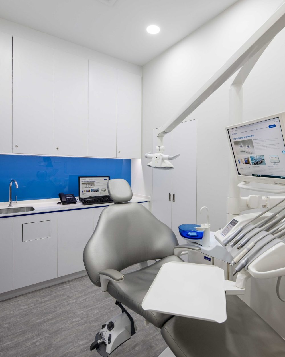 A second treatment room repeats the clinic's signature blue glass backsplash, fitted out with full dental equipment and a patient-facing display scree