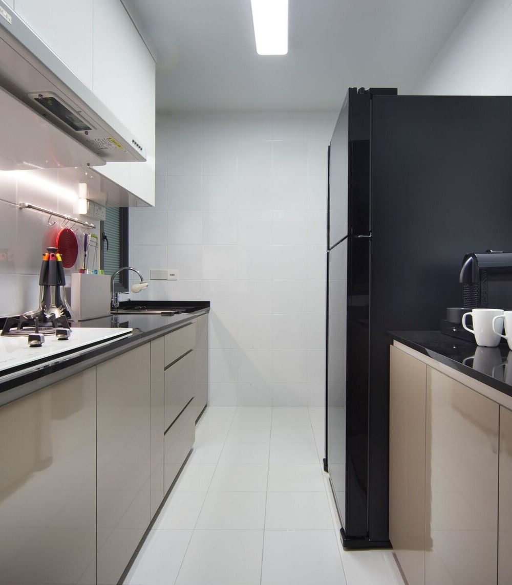 A black refrigerator and taupe cabinetry line the galley kitchen, finished with a black stone counter and a run of white subway-style wall tiles.