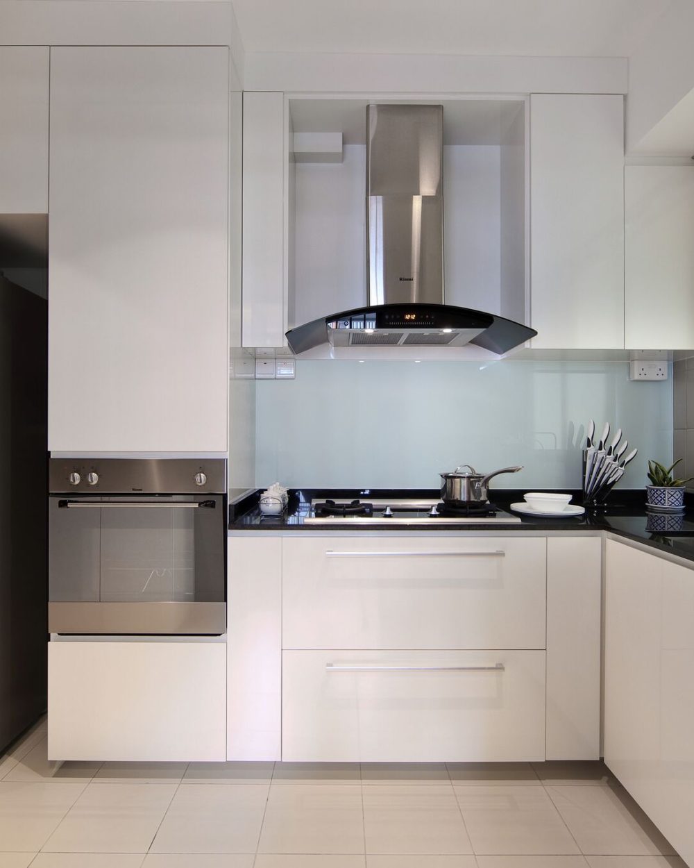 Glossy white cabinetry and a curved stainless steel range hood define the kitchen, paired with a black stone counter and glass splashback.