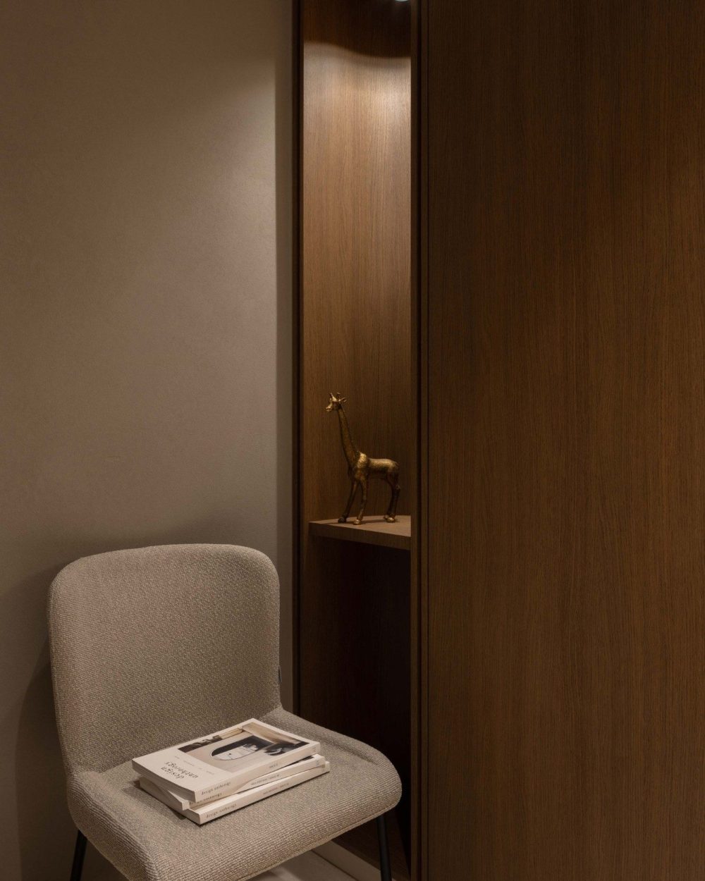 A narrow lit display niche holds a single styled object, a small architectural gesture that breaks up the run of timber wardrobe panelling.