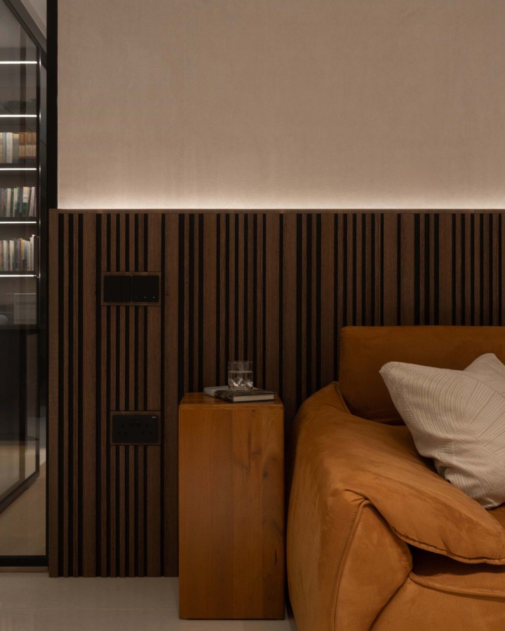 A solid timber block doubles as a side table beside the sofa, set against a fluted wood-panelled wall that conceals the switches and outlets.