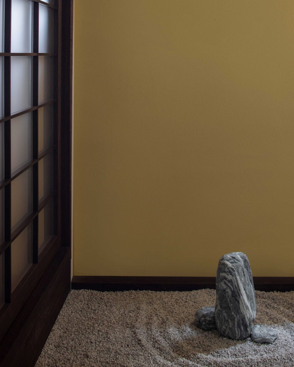 A tall, weathered stone rises from a bed of fine raked gravel, echoing traditional Japanese rock garden design.