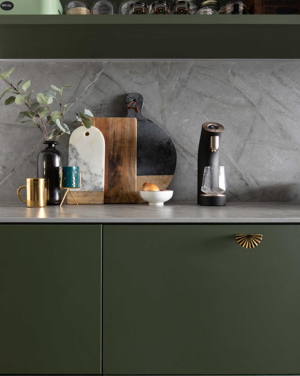 Vintage-style jars, chopping boards and a sleek water dispenser sit against the kitchen's grey marble backsplash.