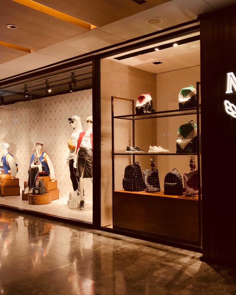 Articulated wooden mannequins model outerwear beside backpacks, sneakers and keychains on shelving.