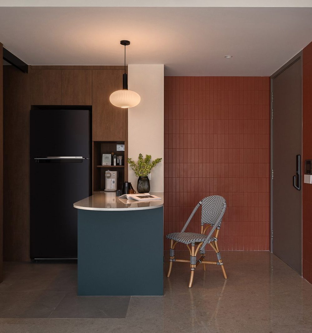 A deep teal island anchors the open kitchen, framed by warm timber cabinetry and the entrance's terracotta feature wall.