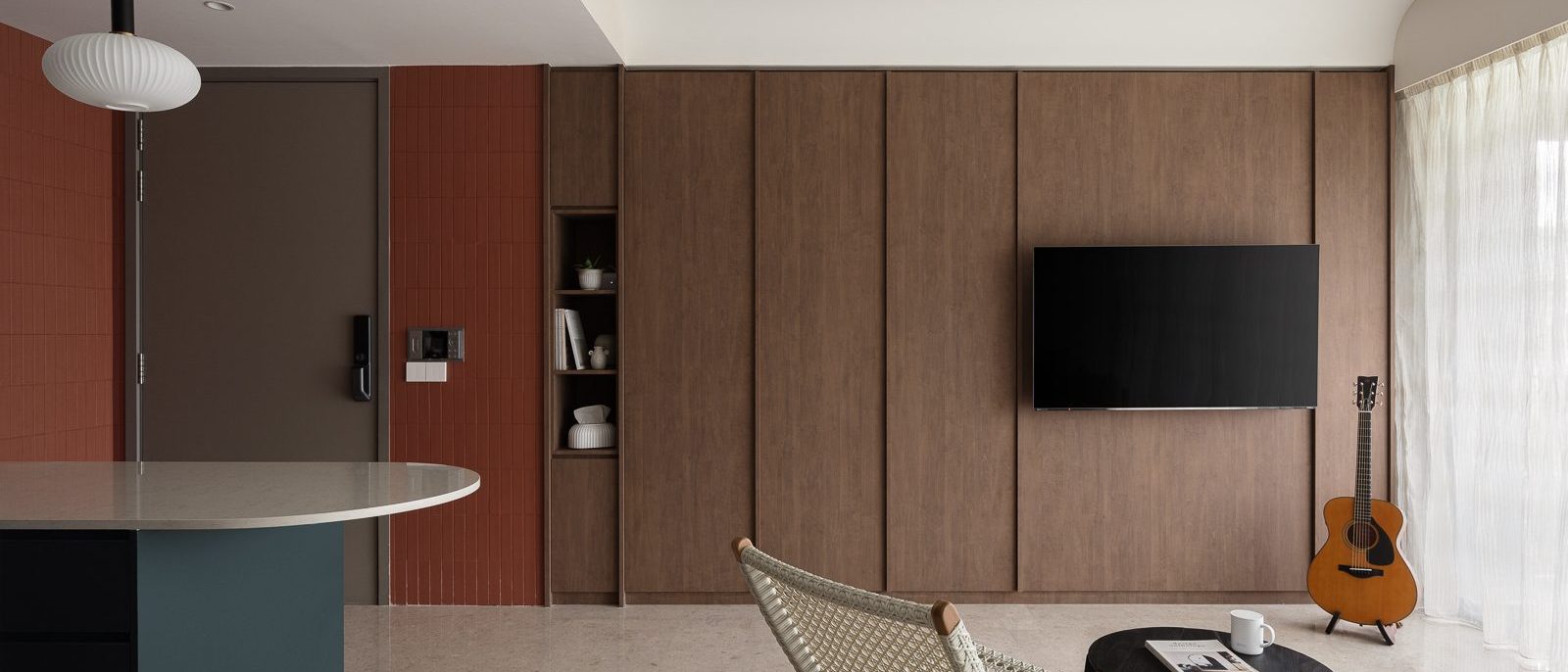 A terracotta tile wall and dark timber TV panel frame the entrance, with a teal kitchen island and woven bistro chair visible just beyond.