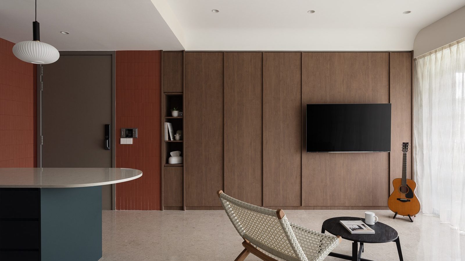 A terracotta tile wall and dark timber TV panel frame the entrance, with a teal kitchen island and woven bistro chair visible just beyond.
