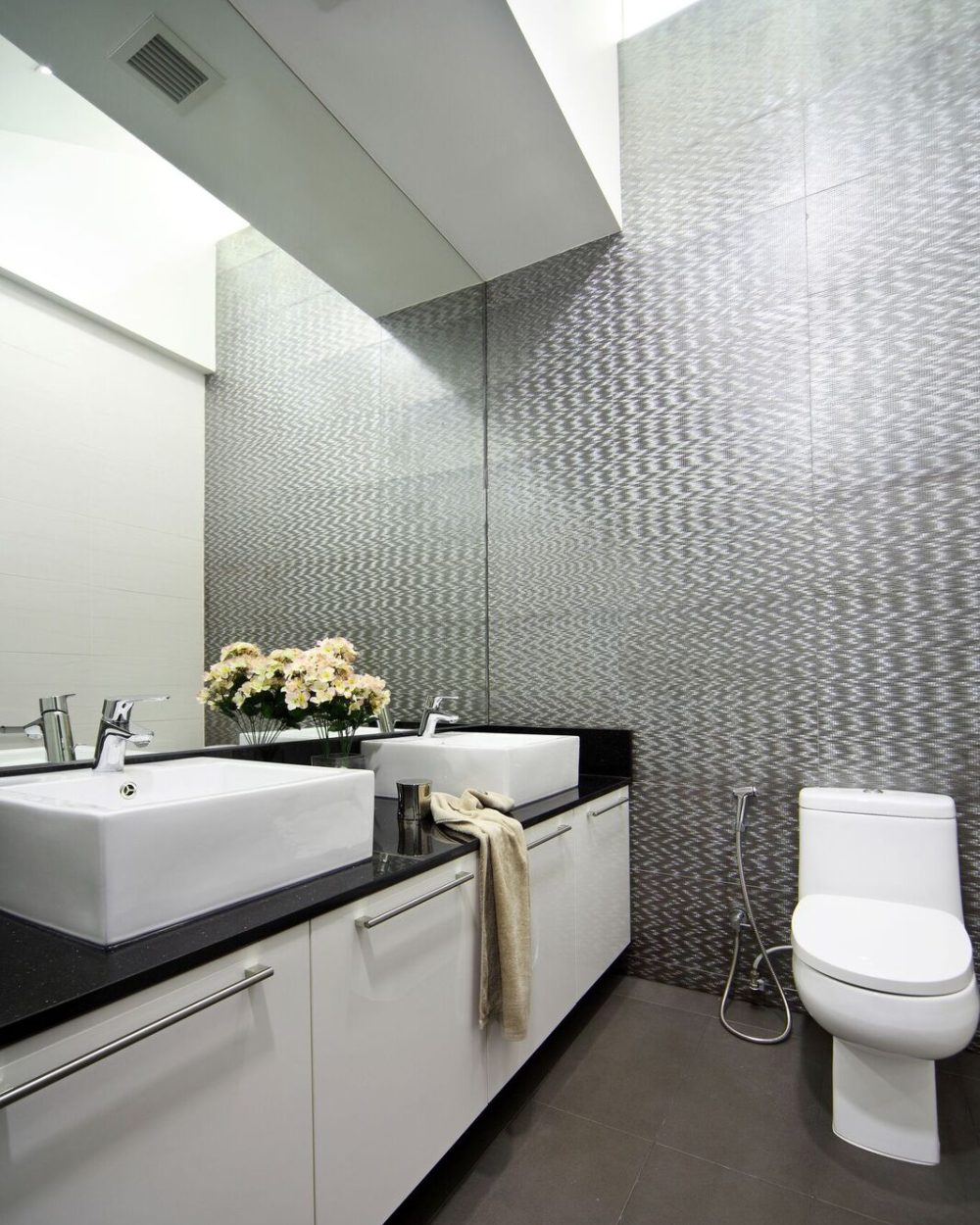 Silver-toned mosaic tiling brings texture to this bathroom, paired with a double vanity and black stone counter.