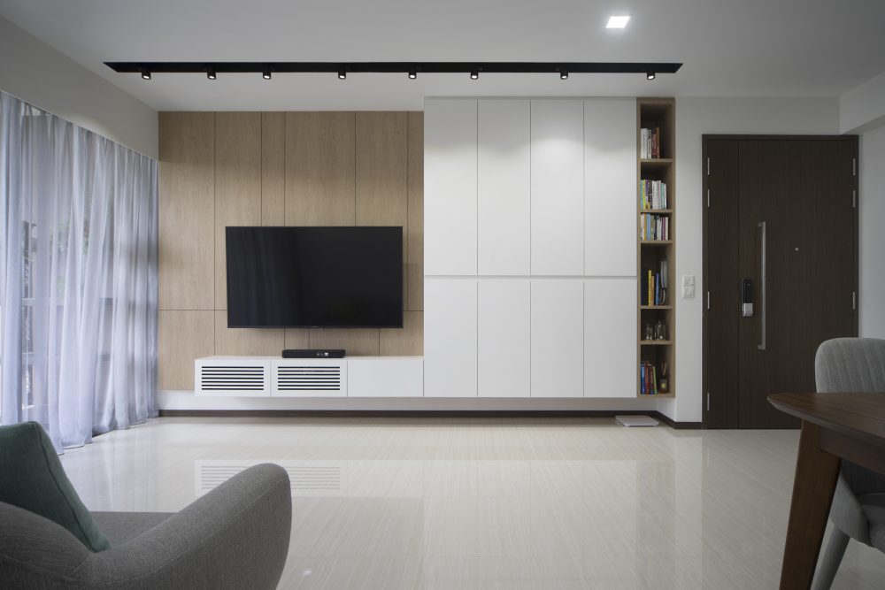 Warm oak panelling meets crisp white storage on the TV wall, finished with an open bookshelf niche beside the front door.