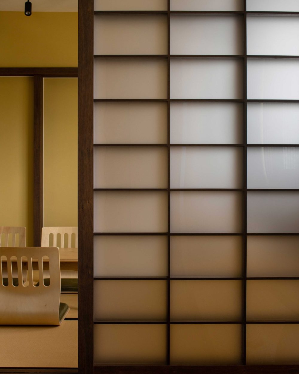 Frosted glass panels set in dark timber grids recreate traditional Japanese shoji screens, filtering soft light into the tea room.