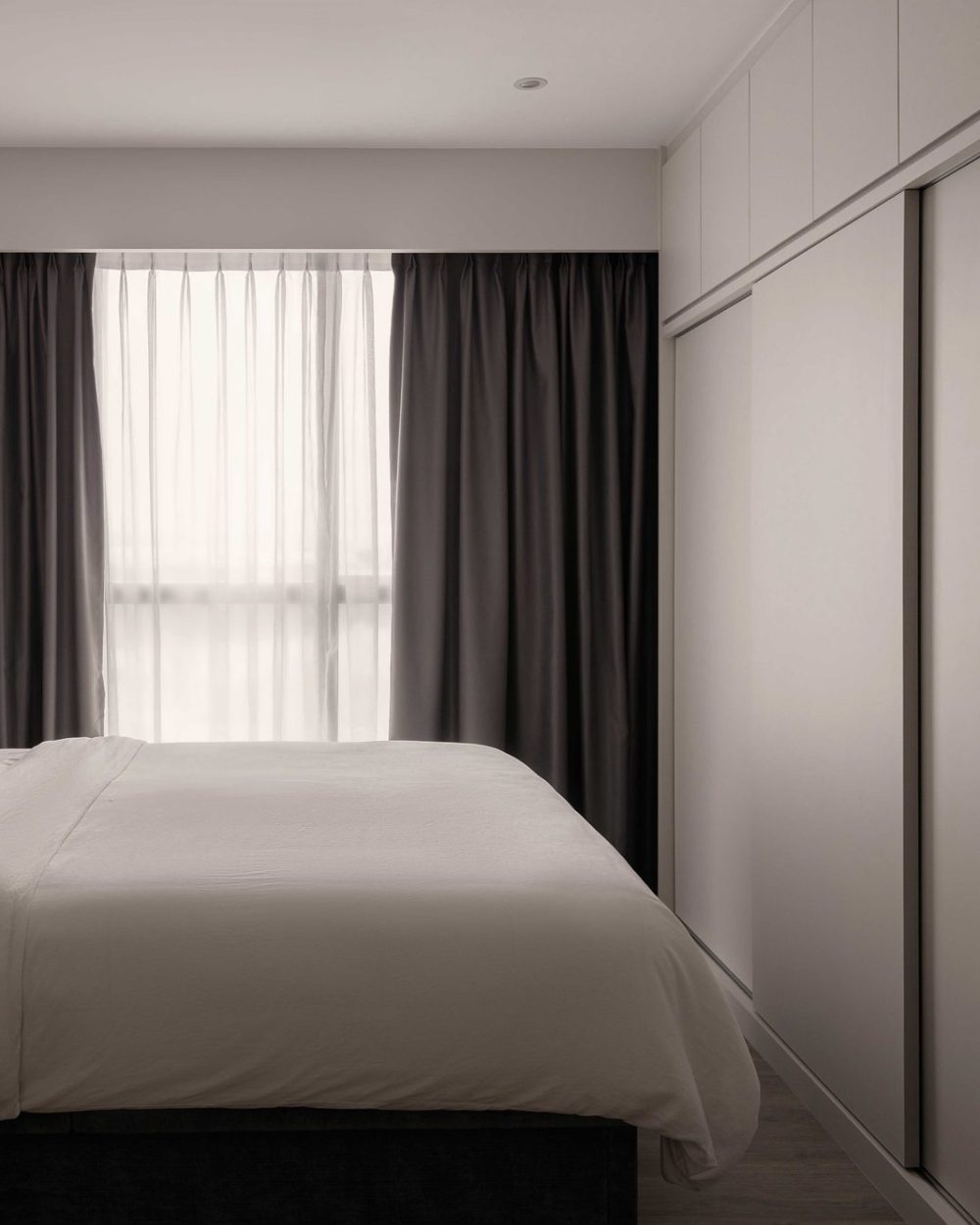 A channel-tufted grey headboard sits beneath floor-to-ceiling curtains, paired with sliding wardrobe doors along the opposite wall.