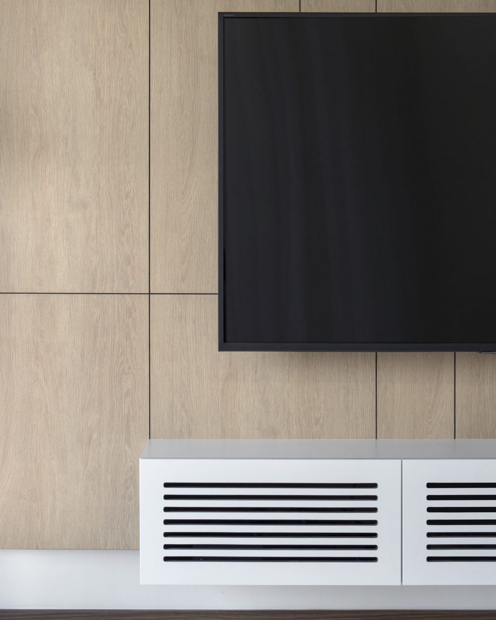 A closer look at the TV wall's slatted vent detailing, built into a floating white console beneath the timber panelling.