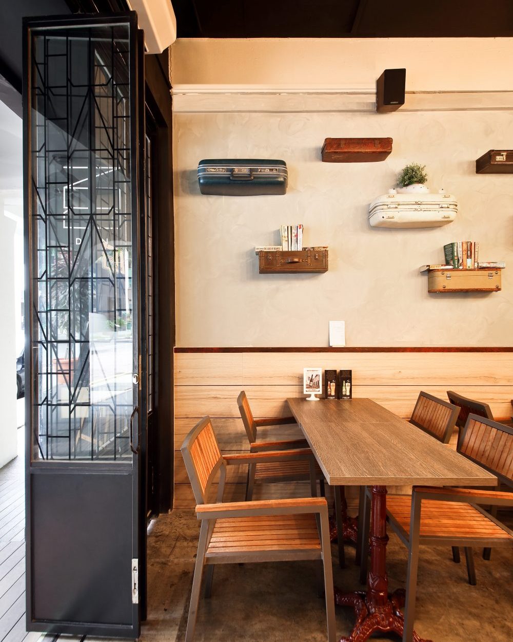 Salvaged vintage suitcases mounted as floating shelves line the wall above industrial metal-and-wood dining chairs.