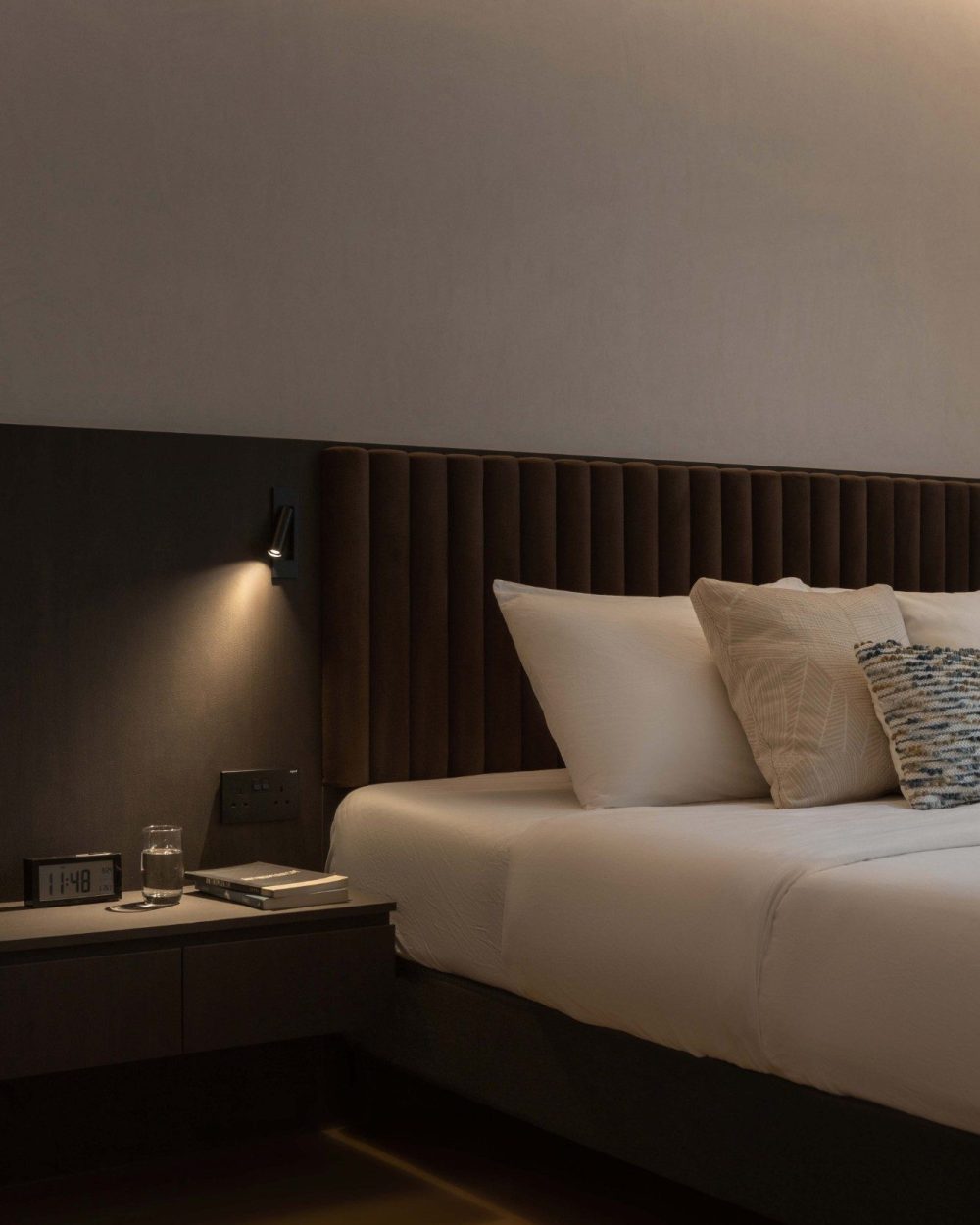 A slim wall-mounted light angles directly over the nightstand, keeping the bedside bright for reading without needing an extra lamp on the surface.