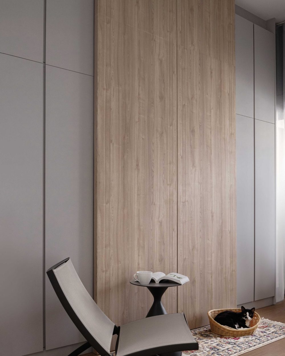 Light oak wardrobe panelling lines a corridor styled with a sling chair and patterned rug — complete with a woven basket for the household cat.