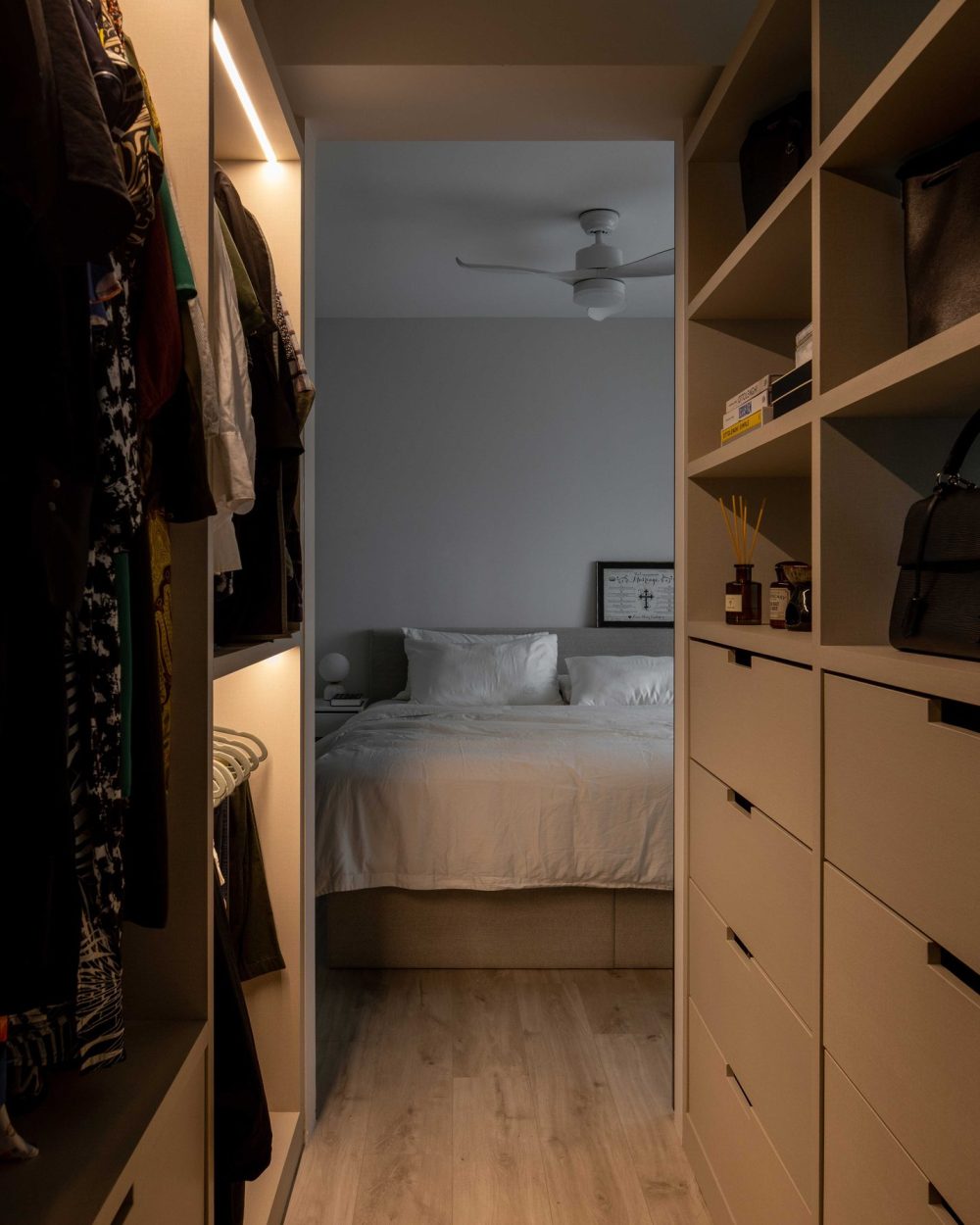 Open shelving lines both sides of the wardrobe corridor, framing a direct view through to the bedroom beyond.