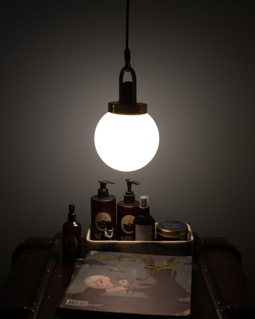 A single pendant bulb lights a small tray of skincare essentials, creating a warm, intimate corner of the bedroom.