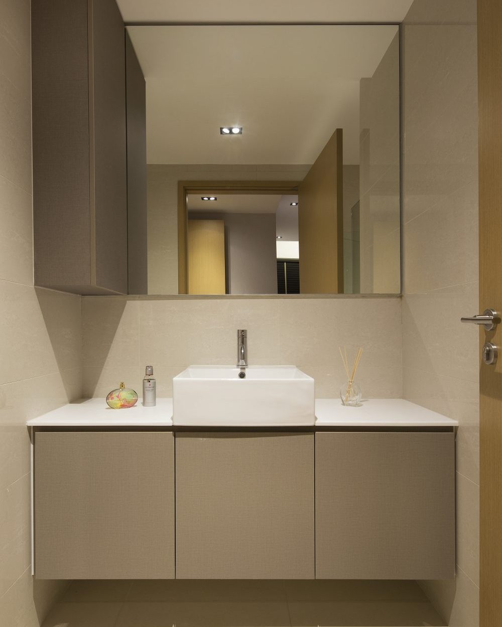 Large-format beige tiles and a full-width mirror keep the ensuite bathroom bright and spacious-feeling.