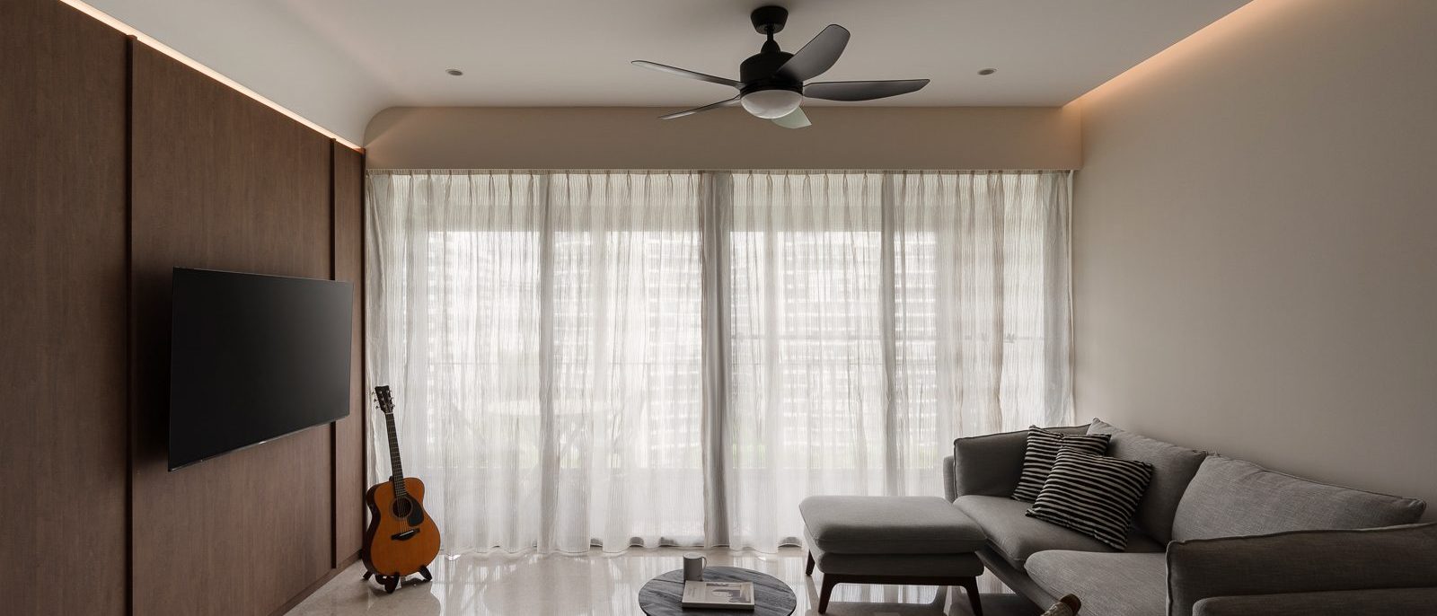A full-height timber panel wall with cove lighting anchors the living room, paired with a grey sectional sofa and sheer curtains.