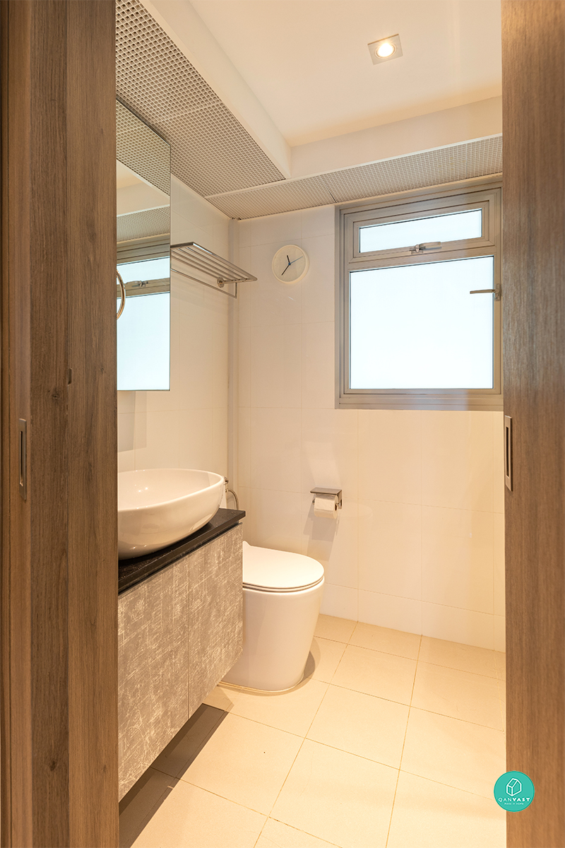 Timber-framed doors and a vessel sink with a dark stone counter bring warmth to the bathroom, lit by a large frosted window.