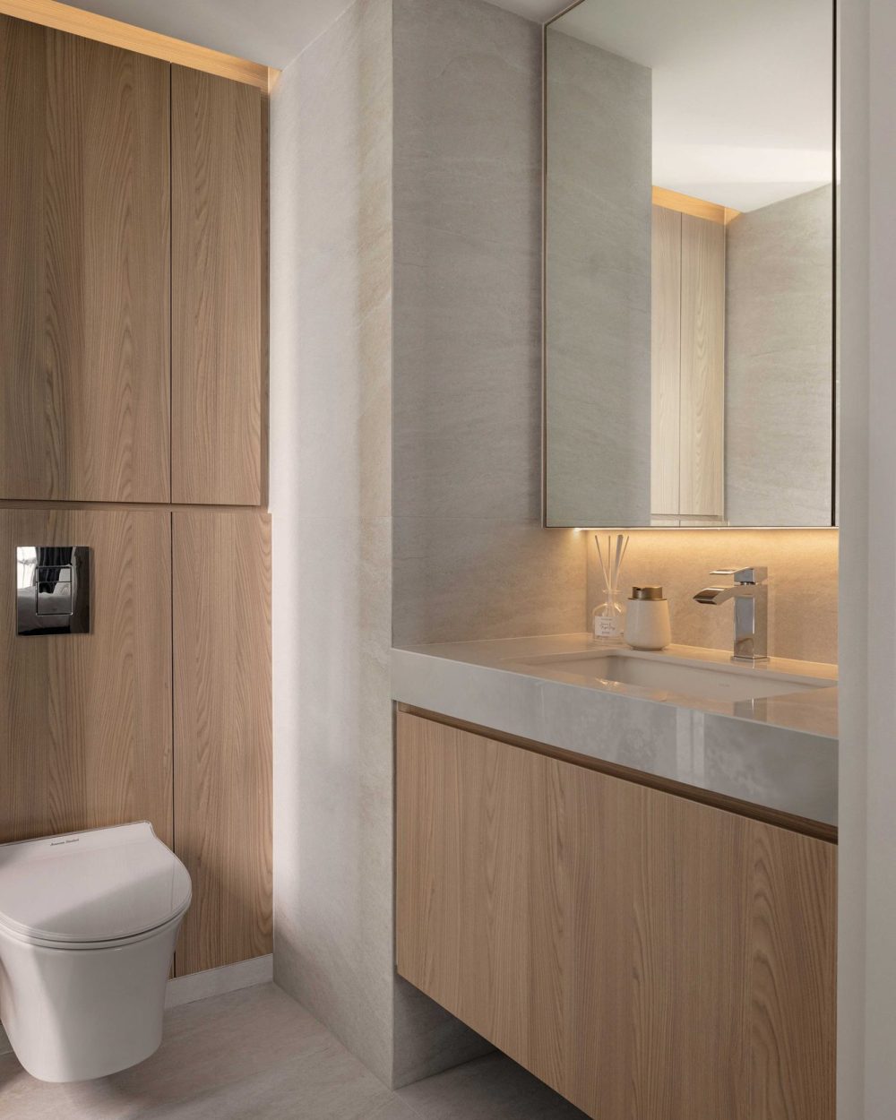 A floating timber vanity and wall-hung toilet keep this powder room feeling open, paired with a backlit round mirror.