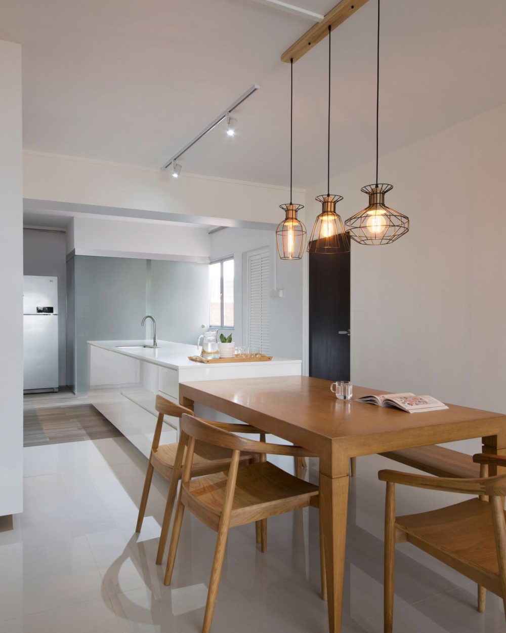 Timber dining chairs and a match-toned table sit beneath the pendant cluster, with the kitchen's stainless fridge visible just beyond.