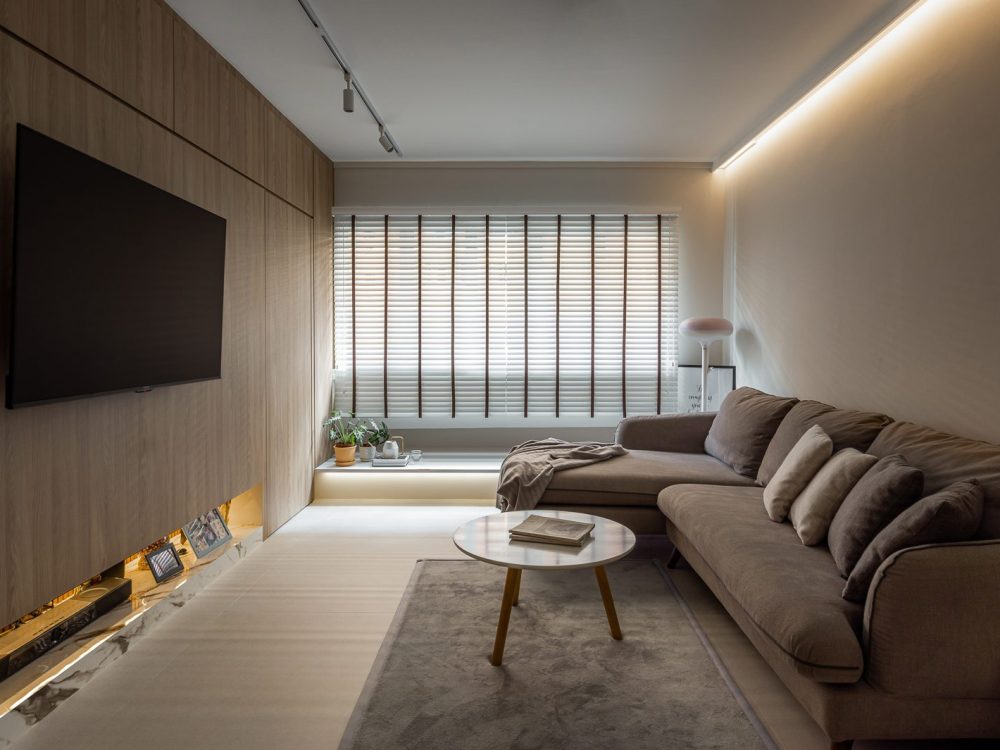 Full-height timber panelling wraps the TV wall, with a backlit marble ledge below for photos and keepsakes, beside a plush sectional sofa.