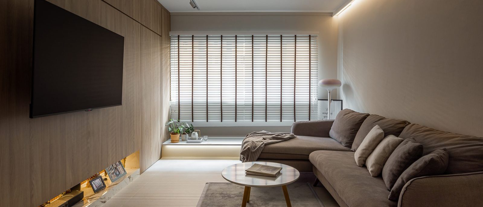 Full-height timber panelling wraps the TV wall, with a backlit marble ledge below for photos and keepsakes, beside a plush sectional sofa.