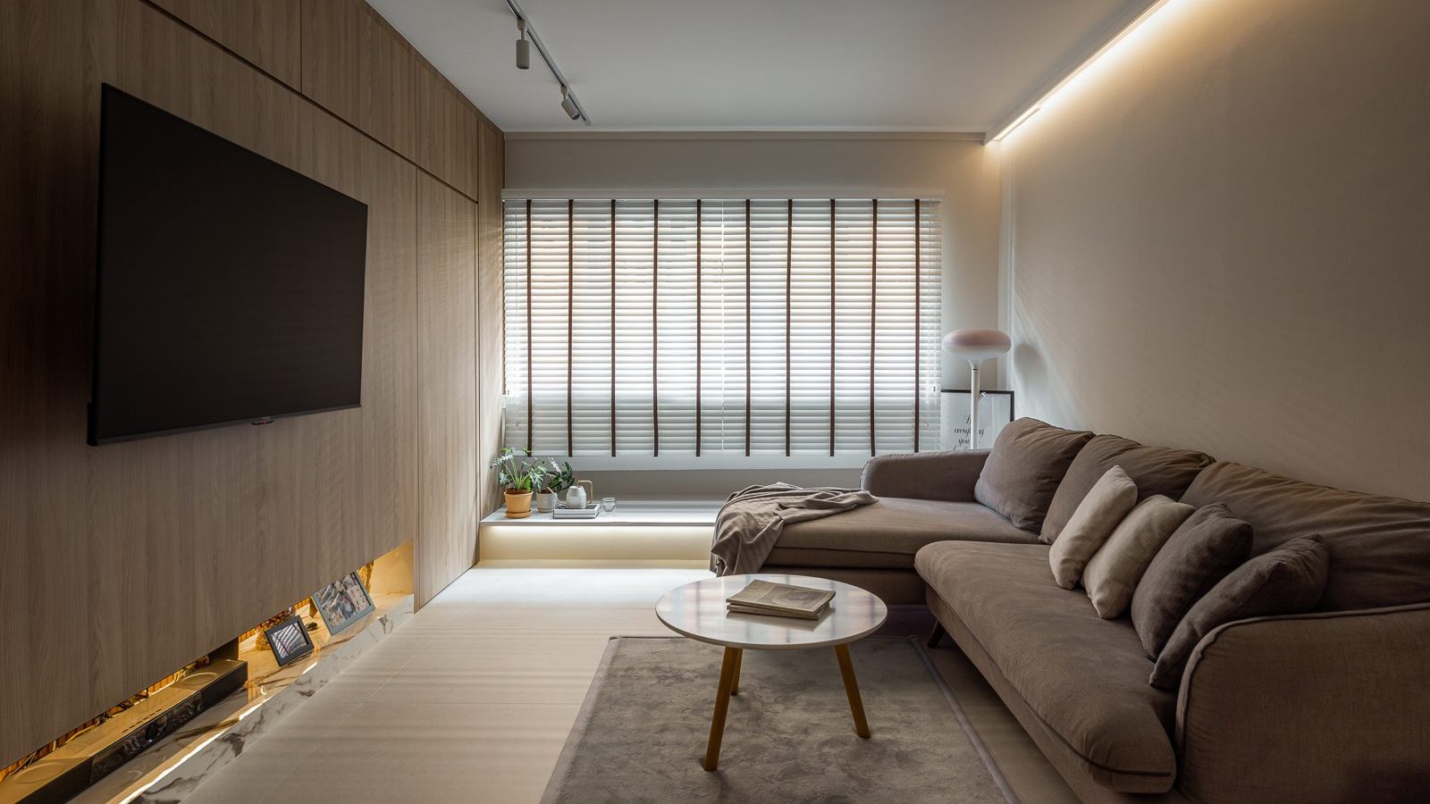 Full-height timber panelling wraps the TV wall, with a backlit marble ledge below for photos and keepsakes, beside a plush sectional sofa.
