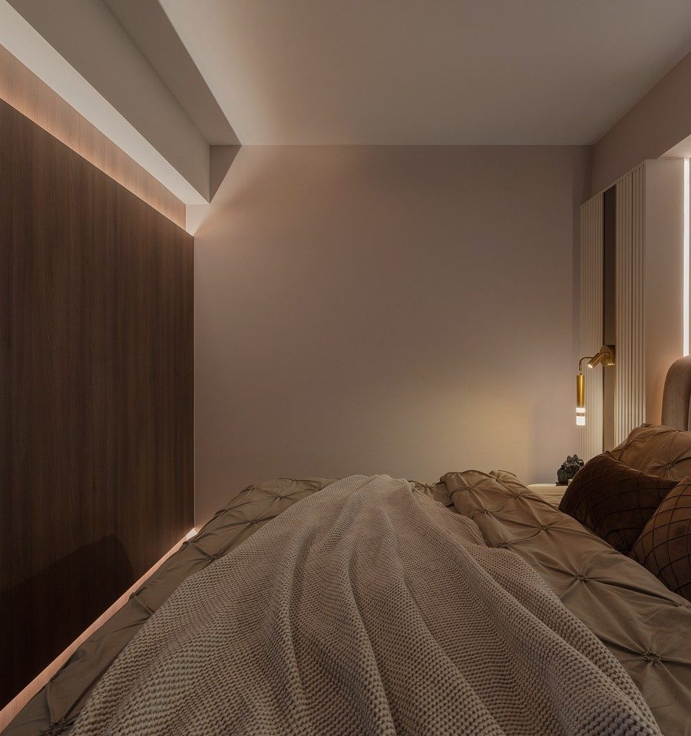 A side angle of the bedroom shows the timber feature wall's cove lighting continuing past the headboard, with a slim fluted wardrobe and brass sconce