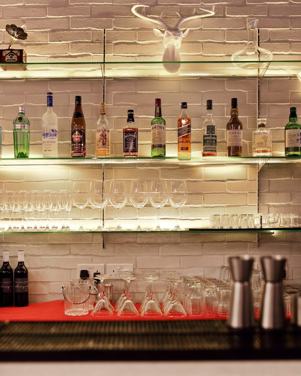Glass shelves lit from below display an extensive spirits collection, topped with a whimsical white stag's head mount.