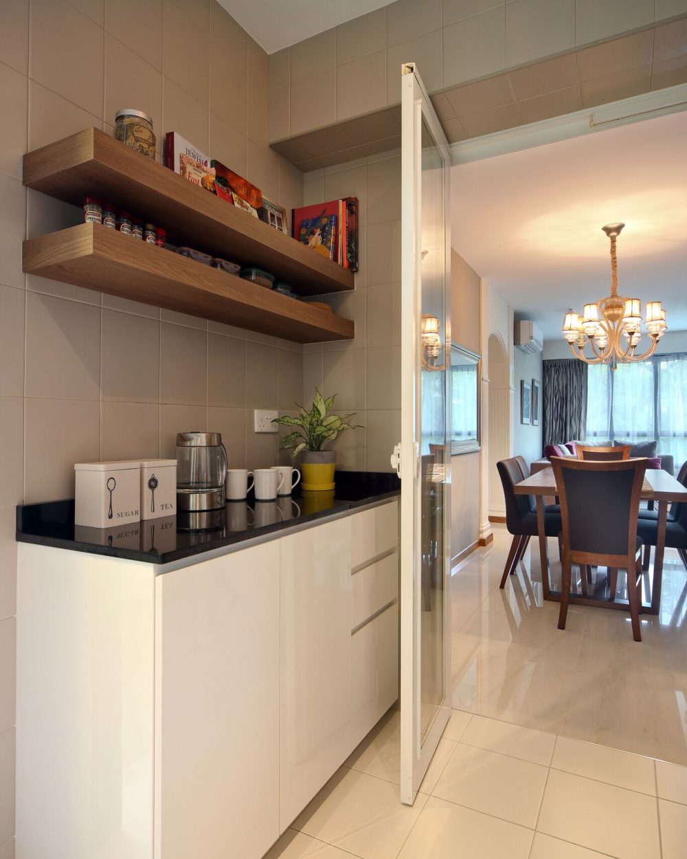 Open timber shelving and a black stone counter form a small servery corner, opening directly onto the dining room beyond.