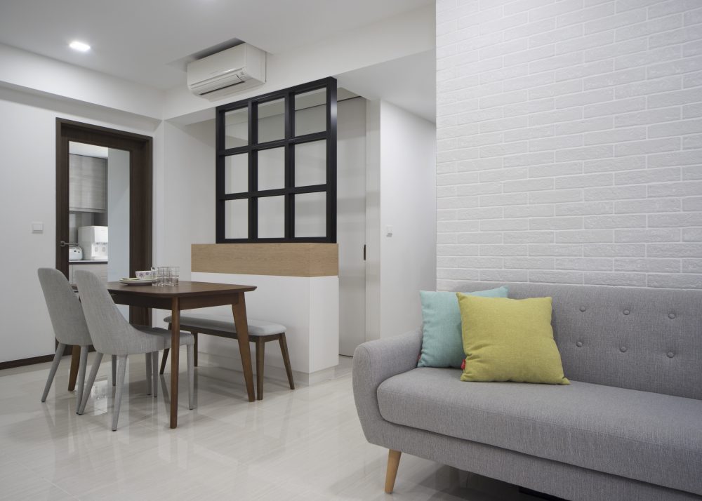 A textured white brick-effect wall brings tactile interest to the living room, paired with teal and mustard accent cushions.