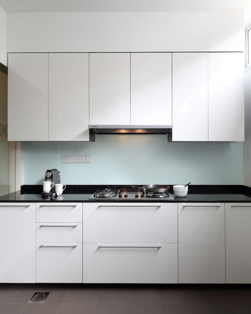 Glossy white cabinetry pairs with a black stone counter and a pale blue glass splashback for a bright, easy-clean kitchen.