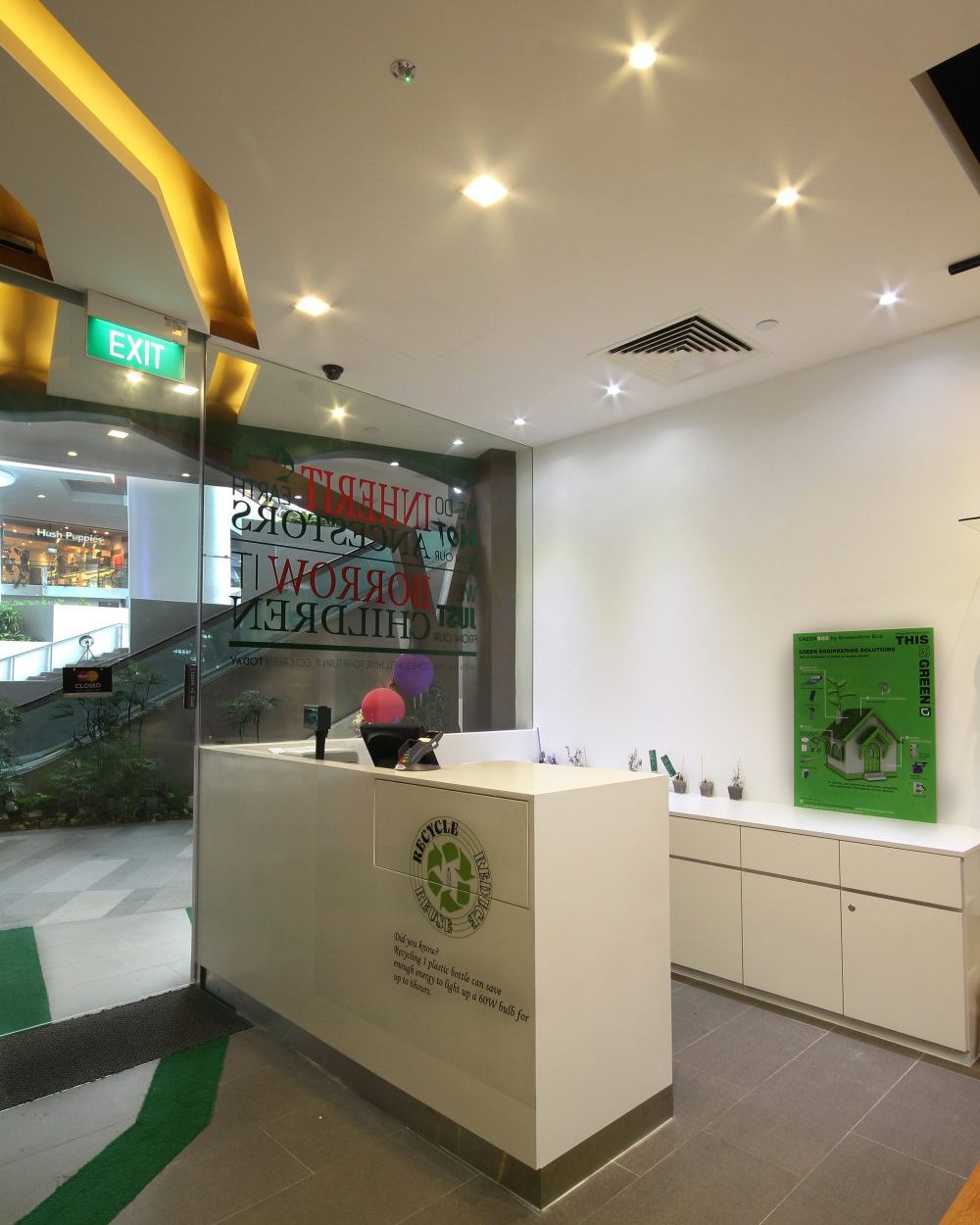 A clean white counter with a recycling emblem greets shoppers at the entrance, backed by informational signage on sustainability.