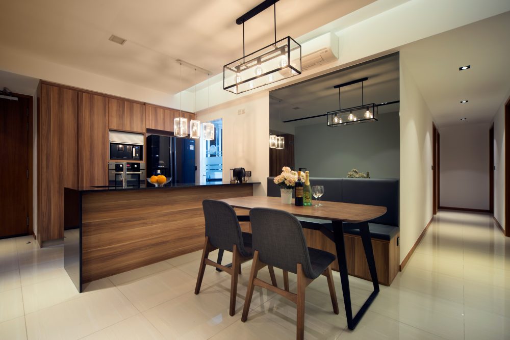 Three cage pendant lights hang over a timber dining table and island, with a built-in bench seat tucked against the dark feature wall.