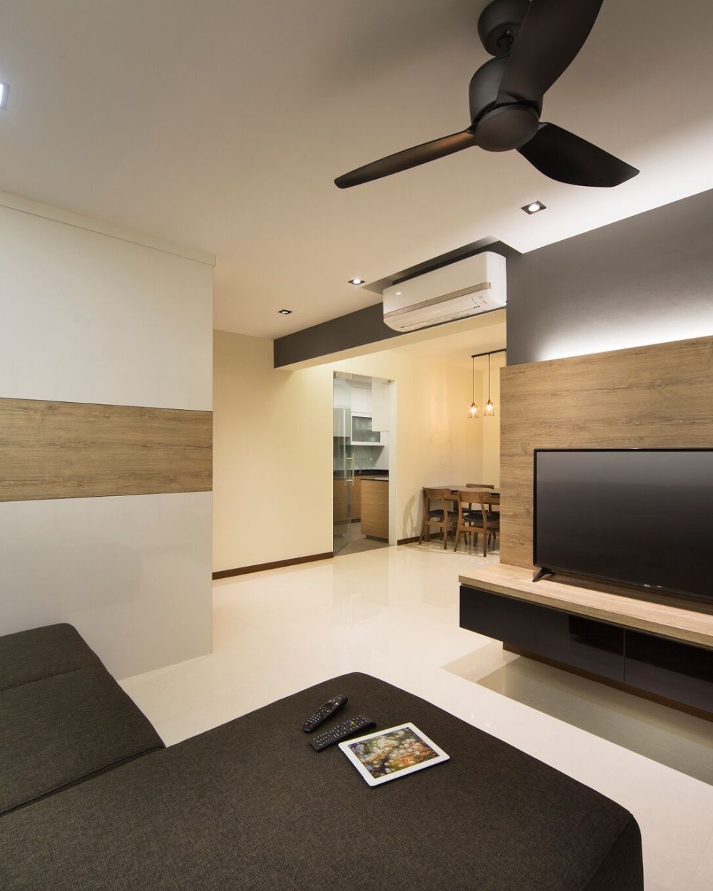 A slatted charcoal-grey and oak-toned wall anchors the TV, with a striped feature wall in the adjoining nook and a wood-panelled dining area beyond.