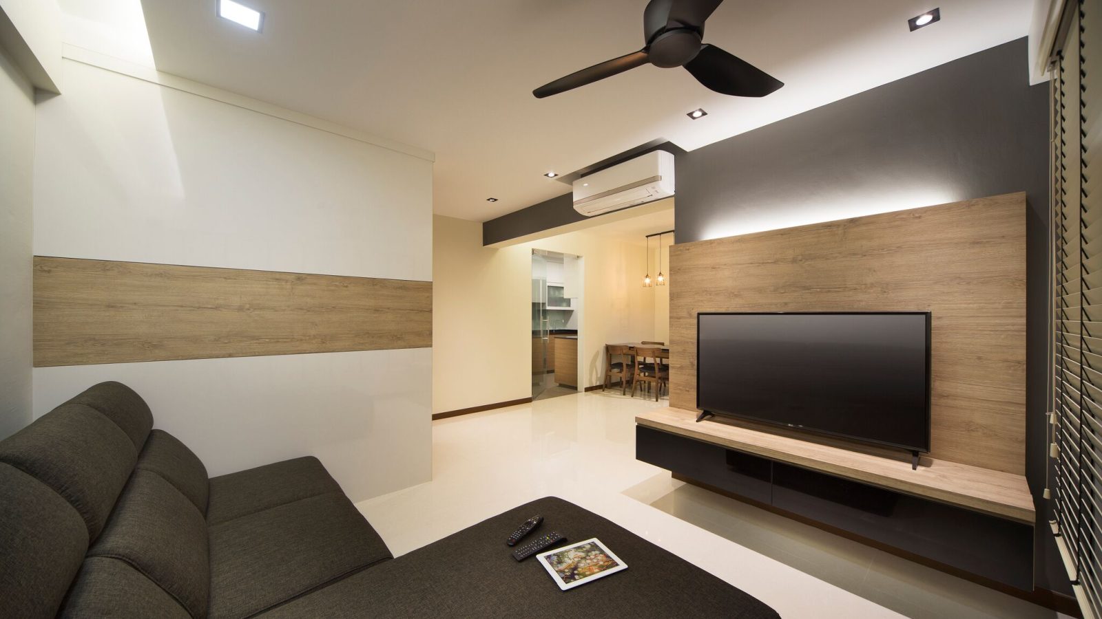 A slatted charcoal-grey and oak-toned wall anchors the TV, with a striped feature wall in the adjoining nook and a wood-panelled dining area beyond.